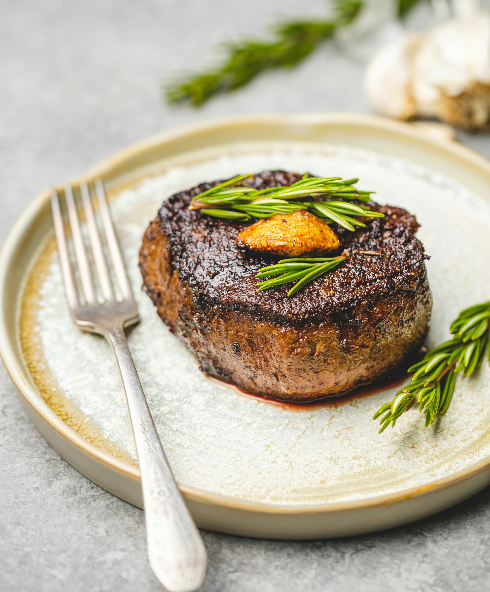 plated filet mignon steak on ceramic plate with rosemary garnish