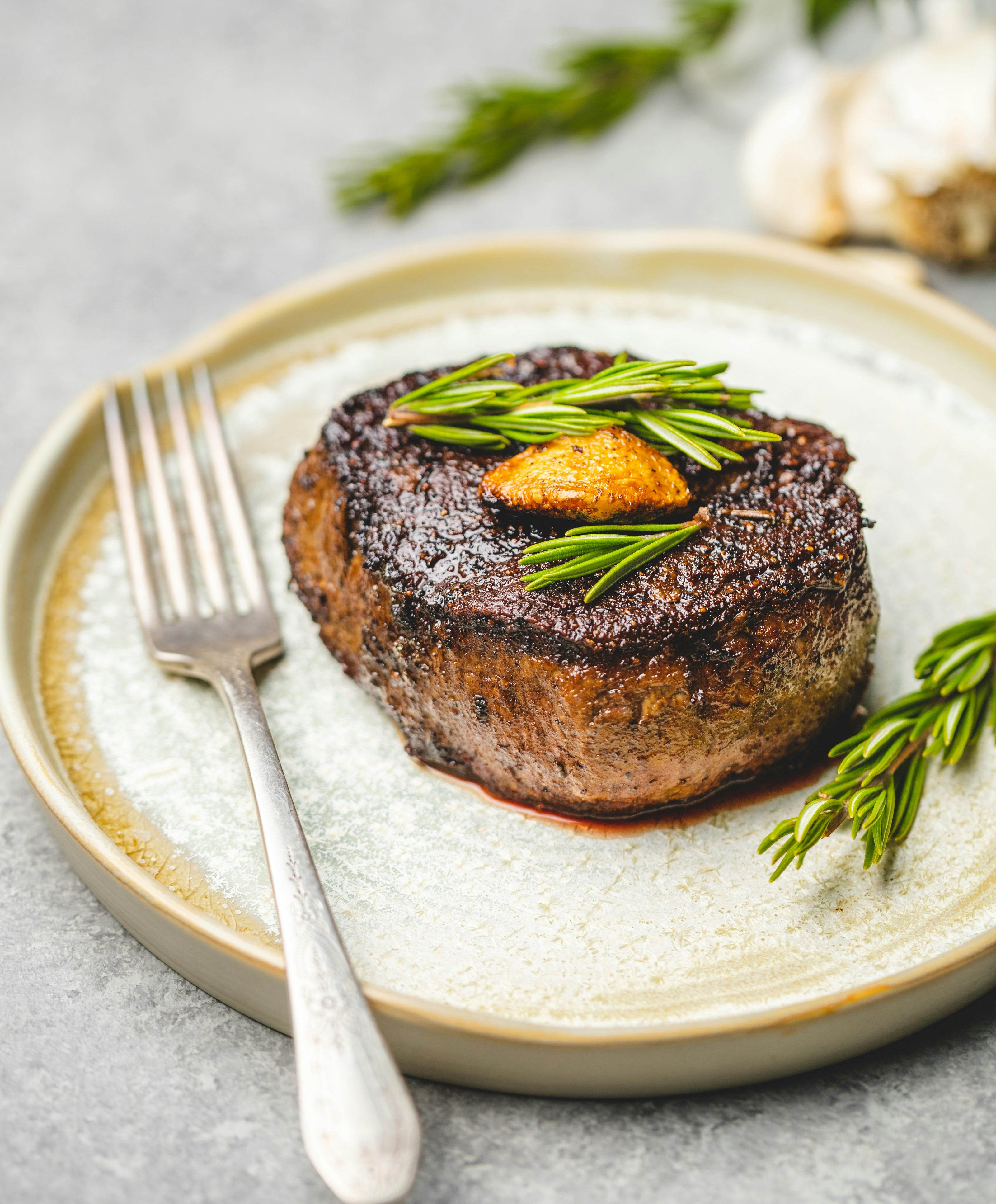 plated filet mignon steak on ceramic plate with rosemary garnish
